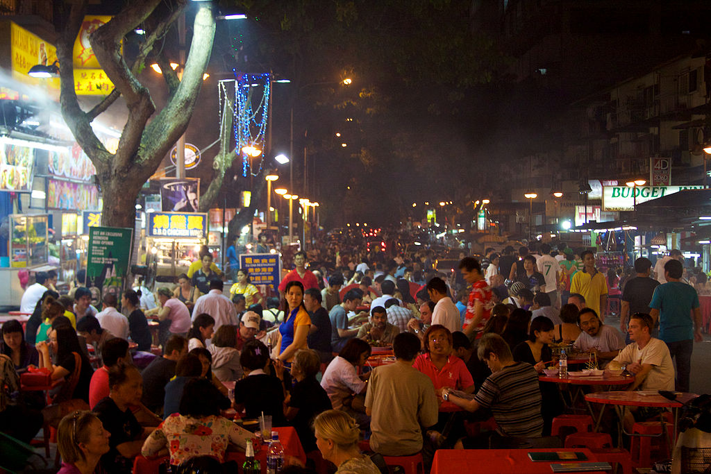 A city street at night filled with crowded tables.