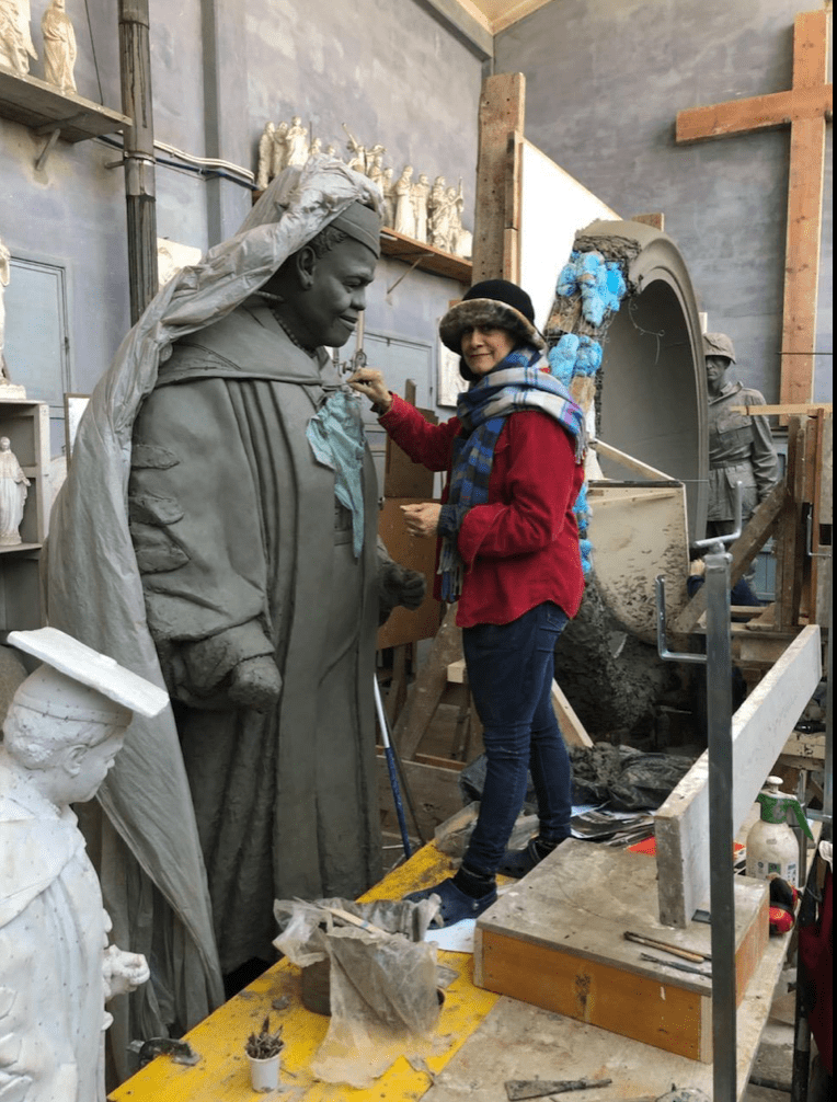 Woman standing on workbench before large clay model of Mary McLeod Bethune in academic cap and gown.